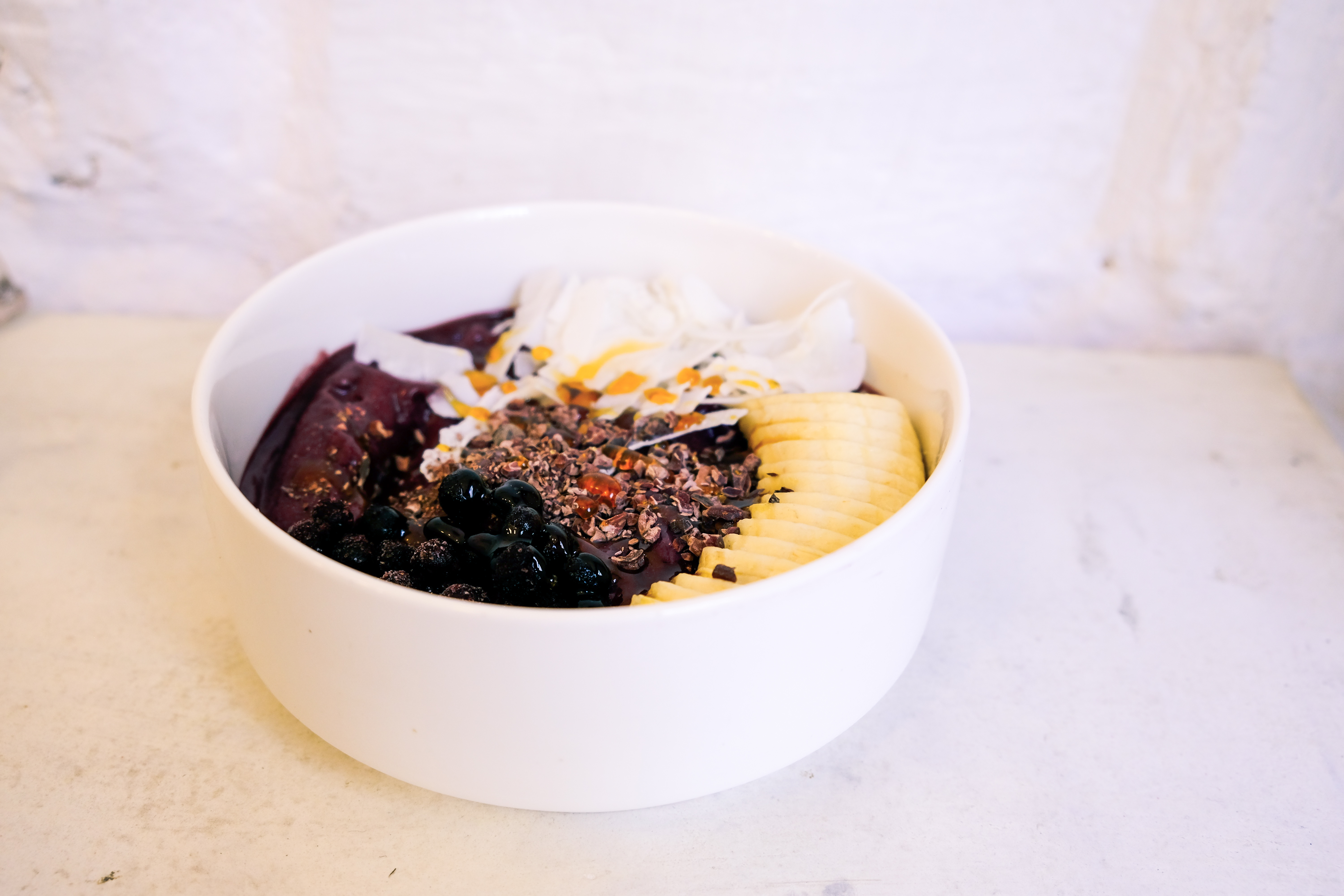 Tigela de açaí com toppings coloridos — granola, frutas e leite condensado — fotografada de cima sobre fundo rústico, representando um item de cardápio digital bem apresentado